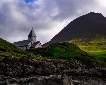 Sacred Heights Viðareiði Church set against a steep mountain under dramatic skies in the Faroe Islands.