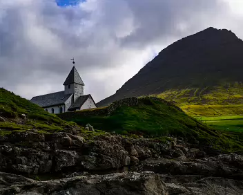 Sacred Heights Viðareiði Church set against a steep mountain under dramatic skies in the Faroe Islands.