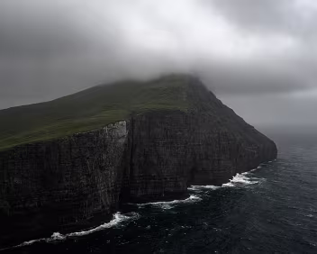 Dark Rise Misty cliff peak at Trælanípa rising steeply from the Atlantic in the Faroe Islands.