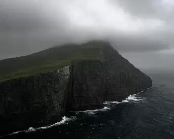 Dark Rise Misty cliff peak at Trælanípa rising steeply from the Atlantic in the Faroe Islands.