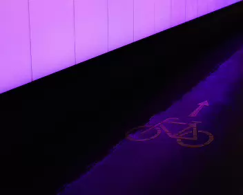 Neon Transit A strip of violet light spills across the asphalt, revealing a faint bicycle symbol pointed into the glow - an abstract hint of motion in a quiet urban...