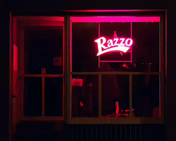 Razzo A storefront glowing in bold red neon, cutting through the darkness of the quiet street.